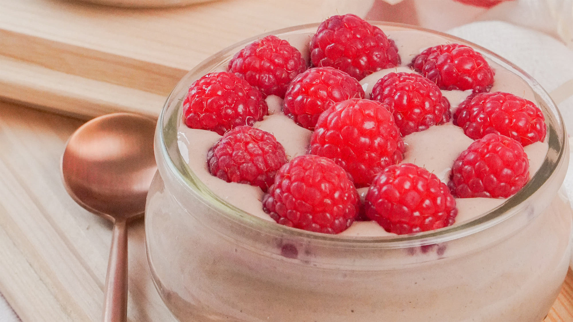 Schoko Pudding im Glas, mit frischen Himbeeren garniert, daneben ein Kupferlöffel