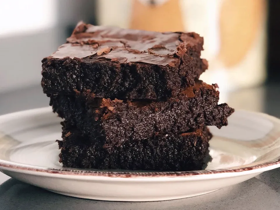 Drei gestapelte Brownies mit dünner, rissiger Kruste auf einem hellen Teller