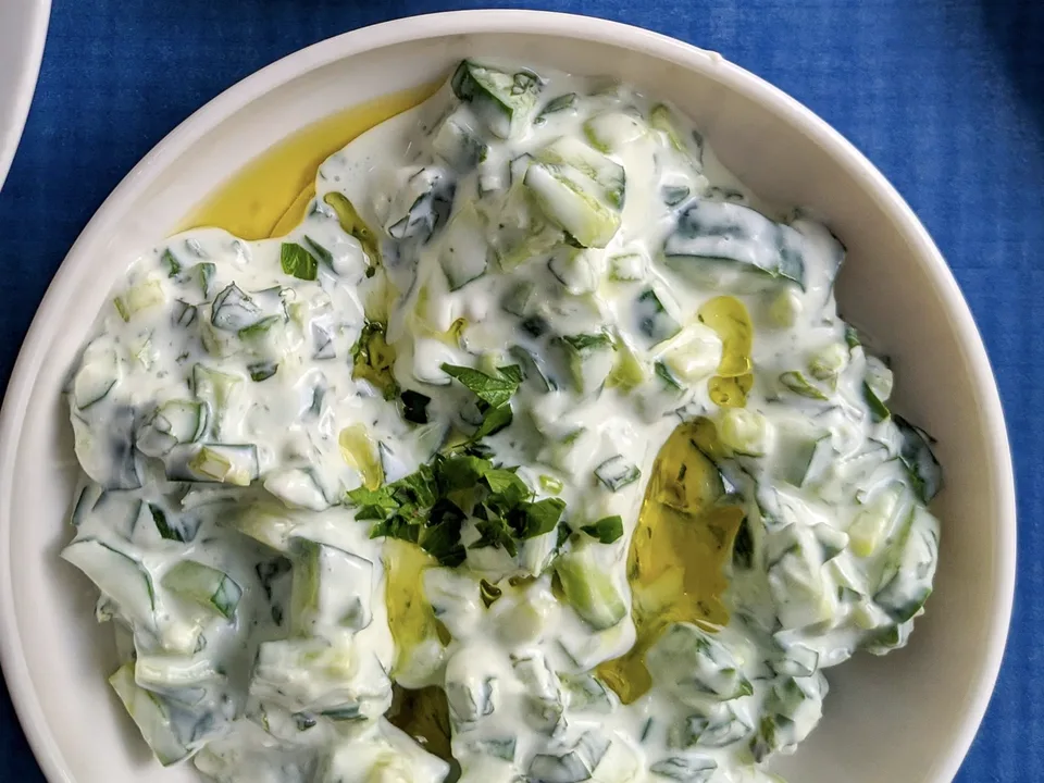 Tzatziki in einer weißen Schale mit Gurkenstücken, Olivenöl und gehackter Petersilie